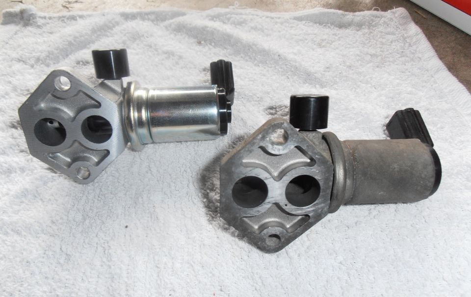 Two idle air control valves, one new and one used, on a white towel