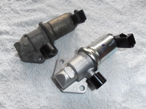 1990 Ford Bronco - A comparison of a used and a new idle air control valve is shown on a white cloth surface.