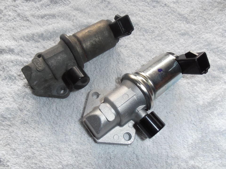 two idle air control valves, one old and one new, on a white towel