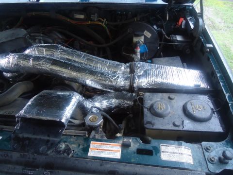 1995 Ford Bronco - The engine bay shows insulated intake pipes and a battery, with visible warning labels on the engine components.