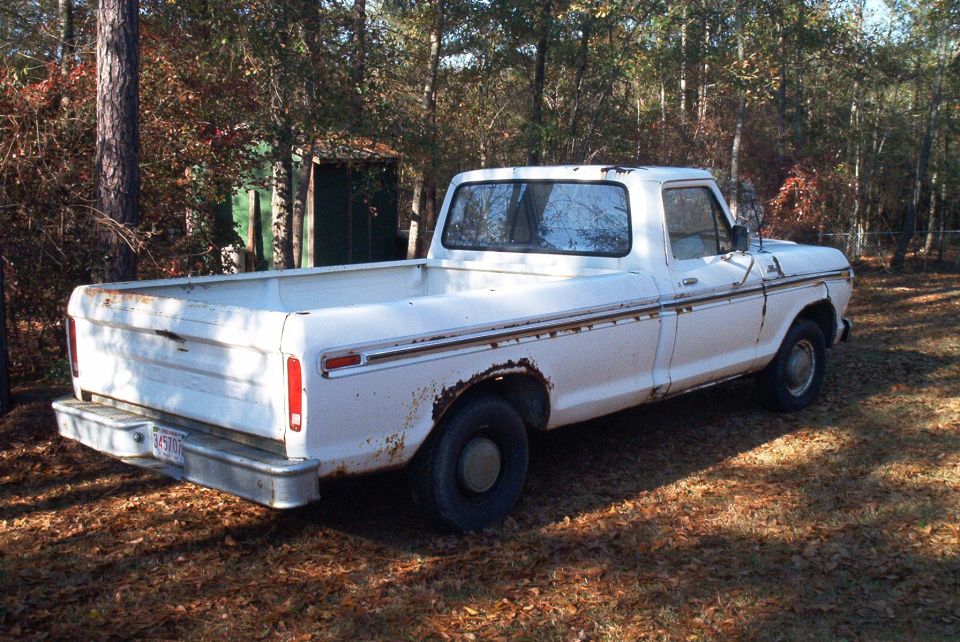 White pickup truck, rear 3/4 view, showing rust and damage on the bed and fender