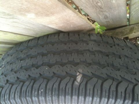 1993 Ford Crown Victoria - A tire is shown resting against a weathered wooden fence with some greenery.