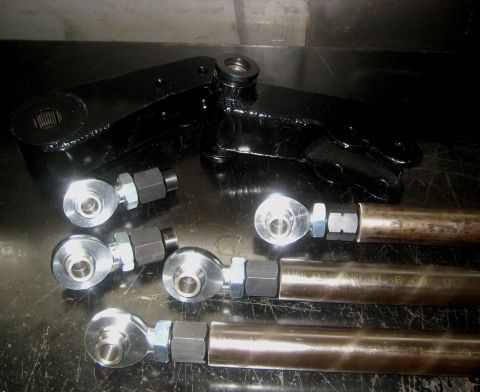 1996 Ford Bronco - Several steering linkage components, including rod ends and a black bracket, are laid out on a dark surface.