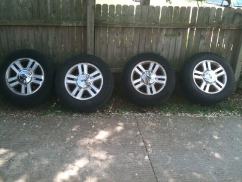 1993 Ford Crown Victoria - Four alloy wheels are displayed in front of a wooden fence, resting on a concrete surface.