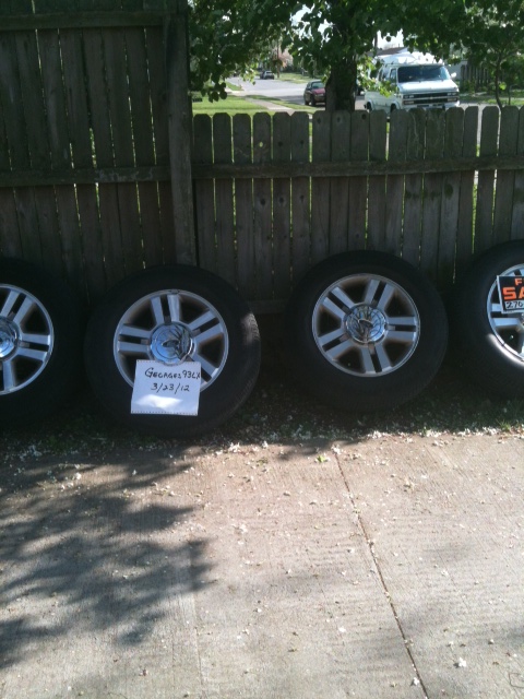 1993 Ford Crown Victoria - Four alloy wheels and tires are lined up against a wooden fence. One wheel has a handwritten note attached.