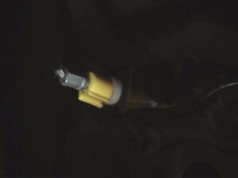1996 Ford Bronco - A close-up view of a throttle cable connection, showing a yellow plastic clip and a metal bolt.