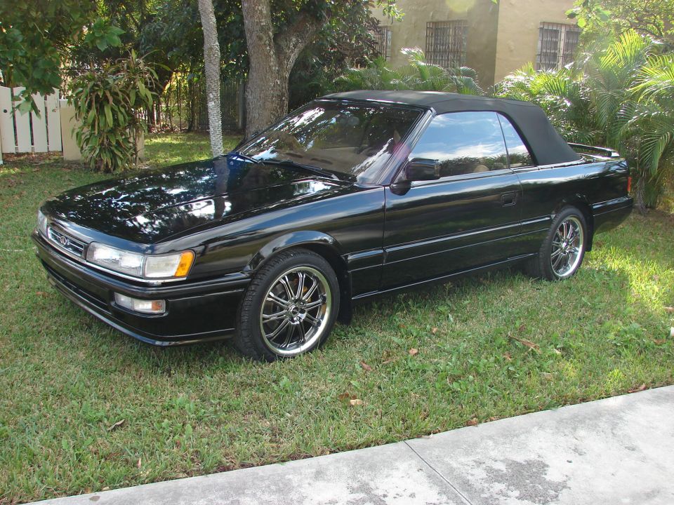 Black Infiniti M30 convertible with soft top up, parked on grass, front 3/4 view