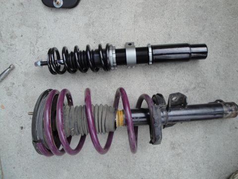 1995 Ford Taurus - Two coilover suspension assemblies, one black and one purple, are displayed on a concrete surface.