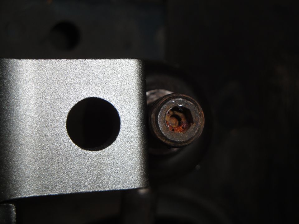 Close-up of a rusted hex bolt head next to a metal bracket with a circular hole
