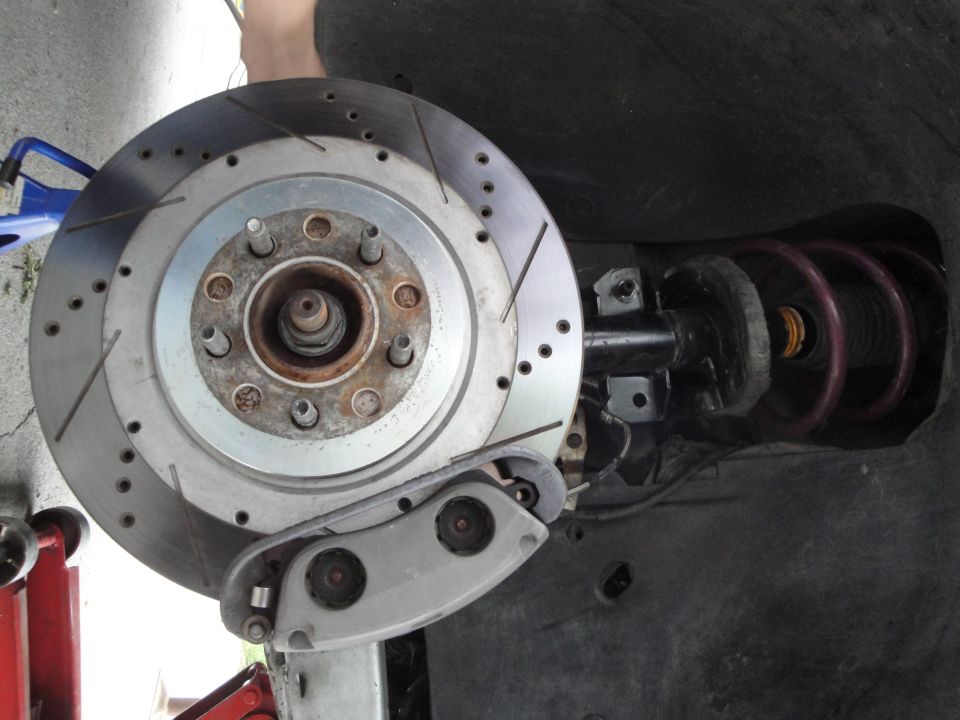 Close-up of a slotted brake rotor, caliper, and coilover suspension assembly