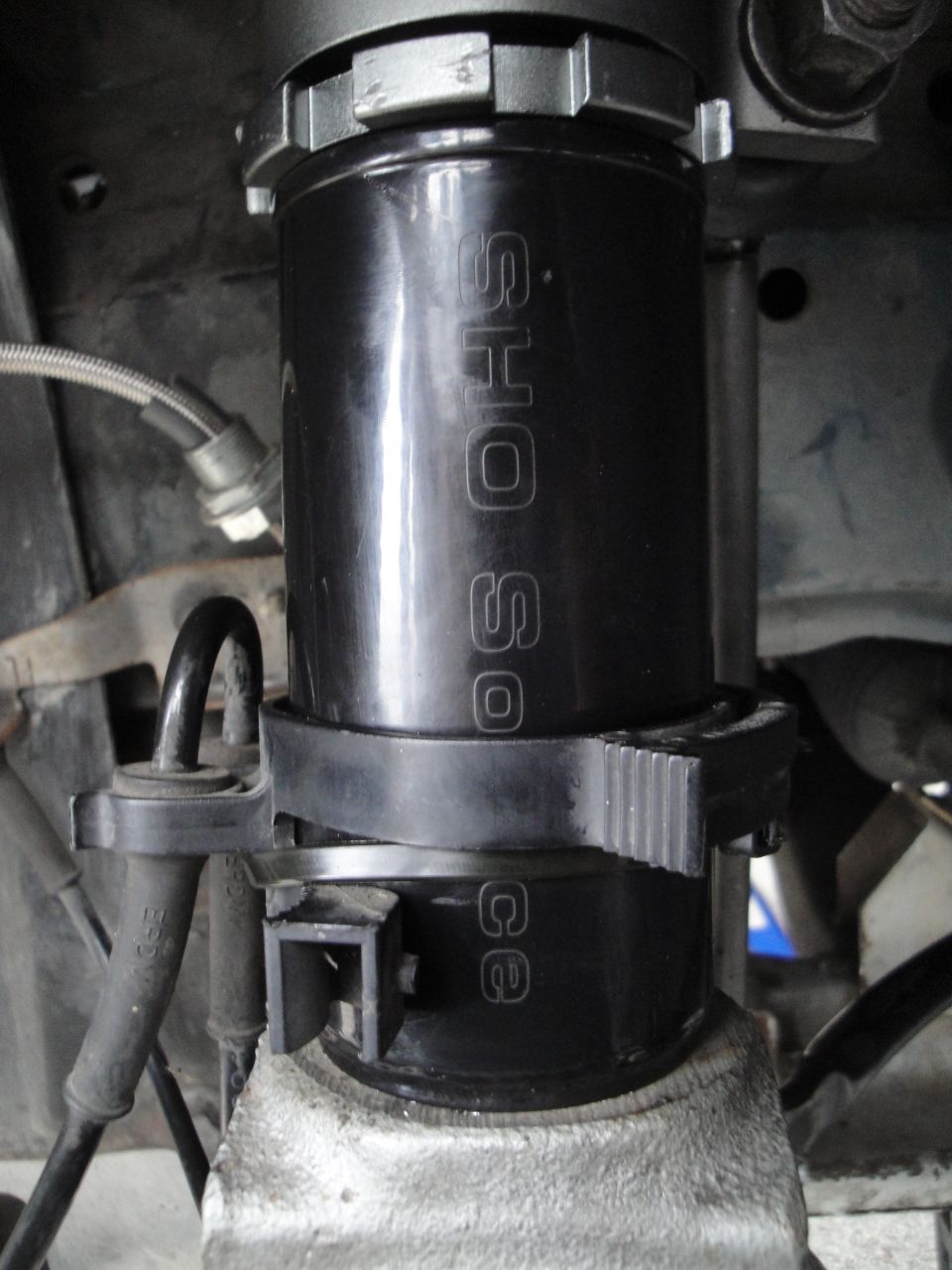 Close-up of a black coilover shock absorber with 'SHO Source' text visible