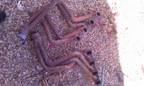 1990 Ford Bronco - Two rusty exhaust manifolds are visible on a gravel surface, with a watermark at the bottom right.