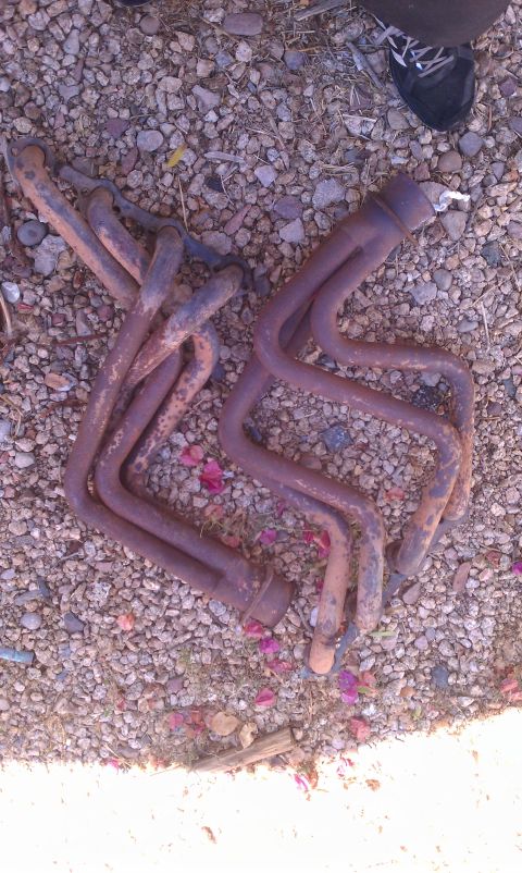 1990 Ford Bronco - A pair of rusty exhaust headers lie on a gravel surface.