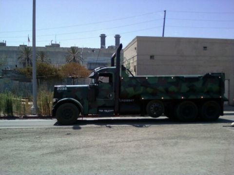 1988 Ford Bronco - A camouflaged dump truck is parked on the side of the road with industrial buildings in the background.