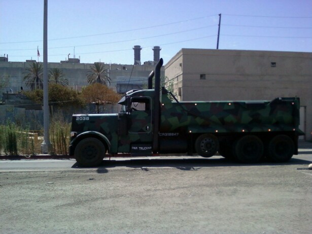 Camouflaged dump truck with dual rear wheels and tall exhaust stacks