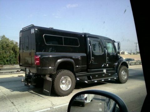 1988 Ford Bronco - A custom black truck with a camper shell is seen from the rear, driving on a highway.