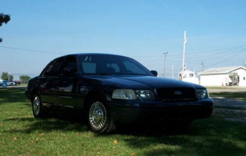 1998 Ford Crown Victoria - A dark-colored Ford Crown Victoria is parked on a grassy area under a clear blue sky.