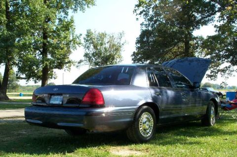 1998 Ford Crown Victoria - A dark blue 1998 Ford Crown Victoria is parked on a grassy field with its hood open.