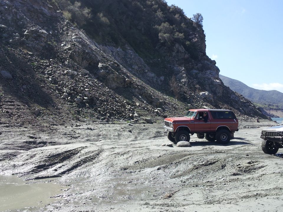 Red 1978 Ford Bronco driving off-road with another vehicle nearby