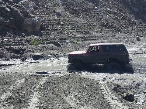 1978 Ford Bronco - A red 1978 Ford Bronco navigates a challenging muddy terrain.