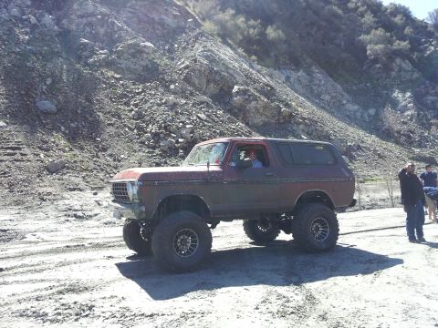 1978 Ford Bronco - A lifted 1978 Ford Bronco is parked on a dirt road, with people standing nearby and a rocky hillside behind it.