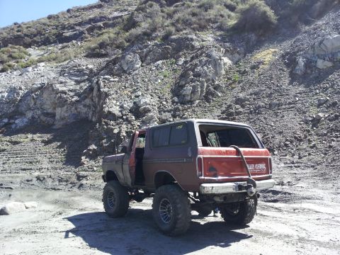 1978 Ford Bronco - A modified 1978 Ford Bronco is seen from a rear three-quarter view on a rocky, off-road terrain.