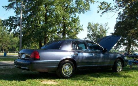1998 Ford Crown Victoria - Side view of a 1998 Ford Crown Victoria with its hood up, parked outdoors.