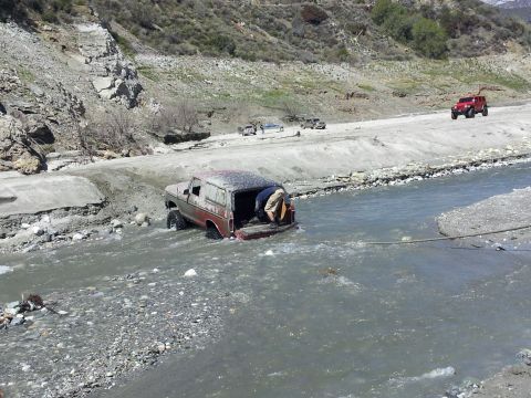 1978 Ford Bronco - A 1978 Ford Bronco is partially submerged in a river while a person attempts to access the cargo area.