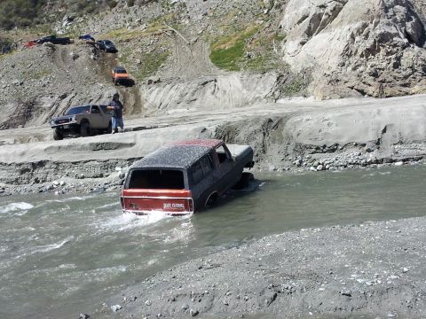 1978 Ford Bronco - A 1978 Ford Bronco navigates a rocky riverbed, with other off-road vehicles visible on the bank.