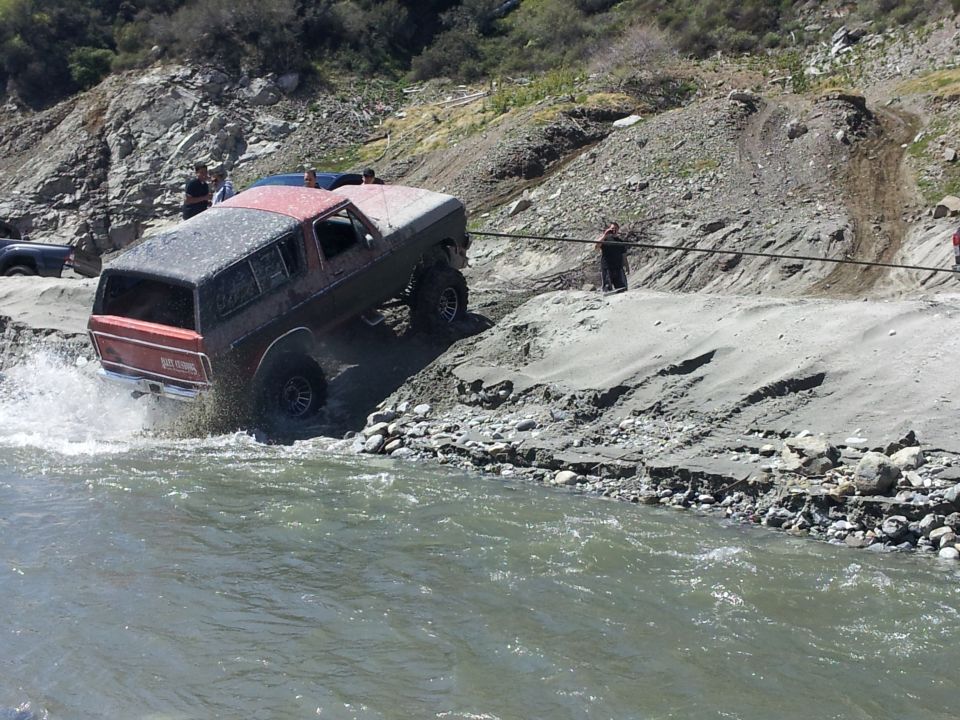 1978 Ford Bronco driving through a river with people watching