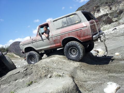 1978 Ford Bronco - 1978 Ford Bronco navigates a challenging off-road terrain with a driver at the wheel.
