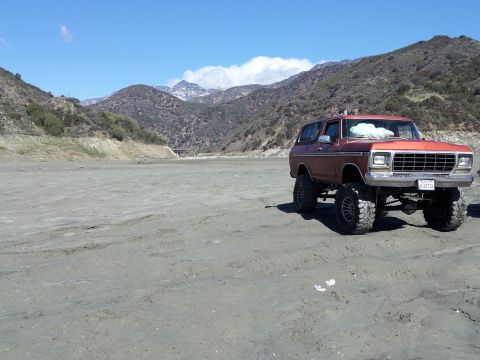 1978 Ford Bronco - A lifted 1978 Ford Bronco sits on a dry lakebed with mountains in the background.