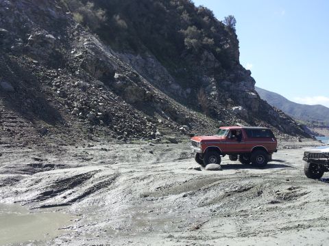 1978 Ford Bronco - A red 1978 Ford Bronco navigates a challenging off-road environment with a rocky hillside and muddy ground.