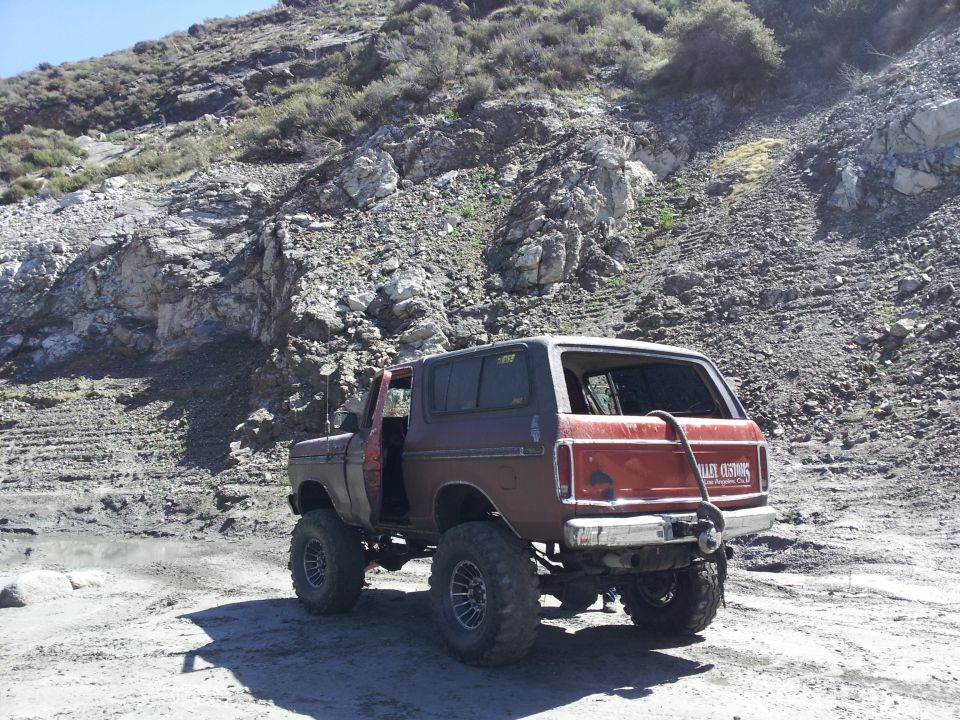 Red and maroon Ford Bronco with lifted suspension and large tires parked on a dirt road