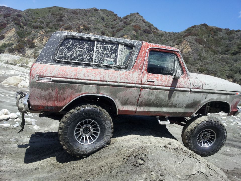 Mud-covered 1978 Ford Bronco with aftermarket wheels on a dirt trail