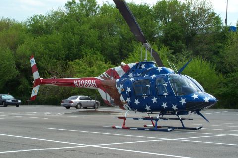 1998 Ford Crown Victoria - A helicopter painted with stars and stripes sits on a tarmac, with two cars parked nearby.