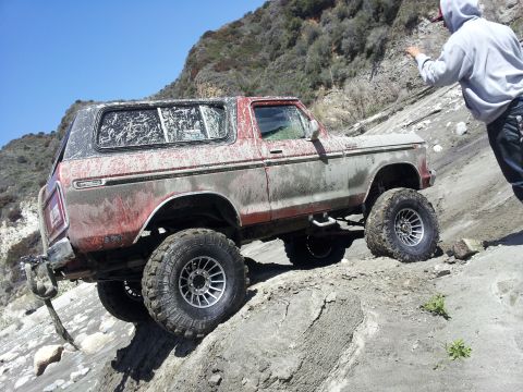 1978 Ford Bronco - A lifted Ford Bronco navigates a challenging off-road trail under a clear blue sky.