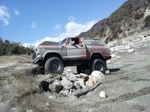 1978 Ford Bronco - A lifted 1978 Ford Bronco navigates a rocky, off-road terrain under a clear blue sky.
