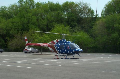 1998 Ford Crown Victoria - A helicopter painted with stars and stripes sits in a parking lot, with a silver sedan nearby.