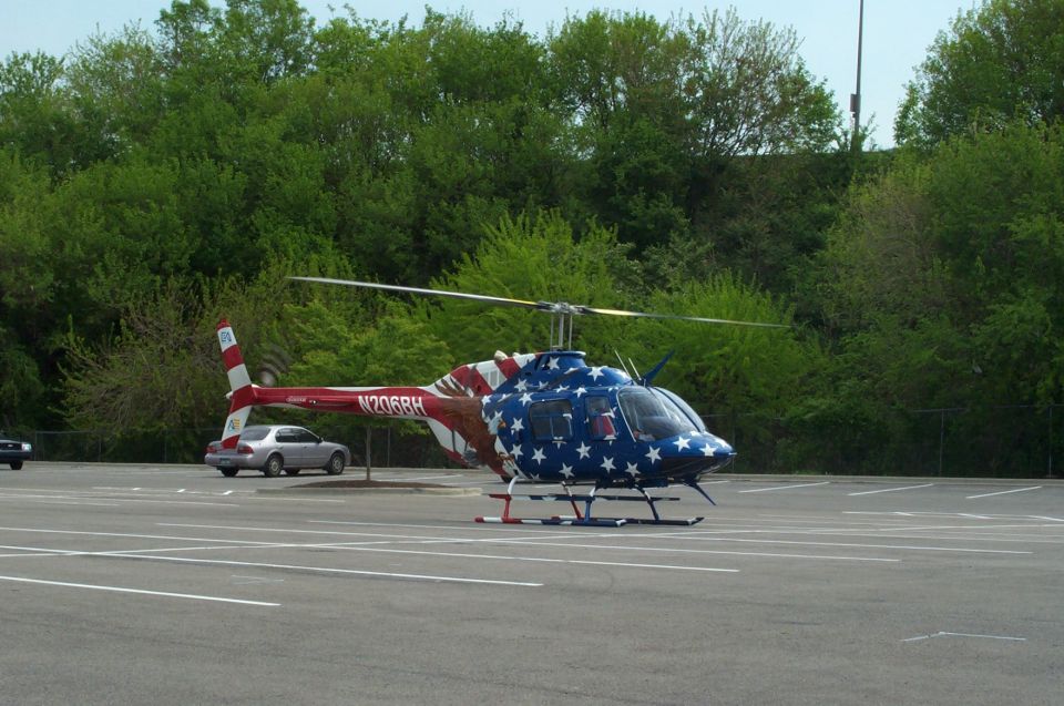 American flag-painted Bell helicopter in a parking lot with a silver sedan behind it
