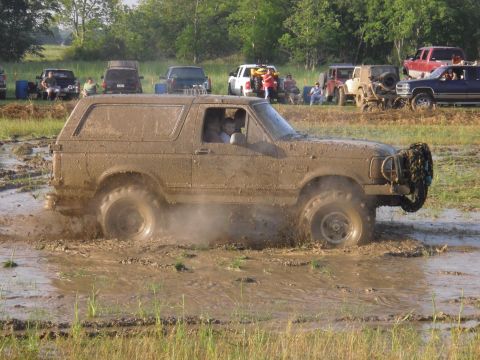 1993 Ford Bronco - A muddy SUV navigates a challenging off-road course with other vehicles in the background.