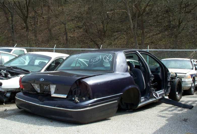 Wrecked dark Ford Crown Victoria in a junkyard, rear quarter and door cut away, soap markings on glass