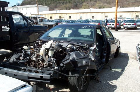 1998 Ford Crown Victoria - Front view of a damaged 1998 Ford Crown Victoria, engine exposed, with a black truck beside it.