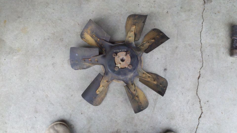Black and yellow metal radiator fan blade with seven blades, resting on a concrete surface