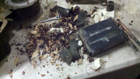 1978 Ford Bronco - Disassembled vehicle heater core and surrounding debris, including leaves and insulation, on a workbench.
