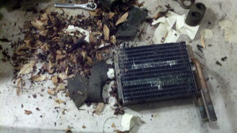 1978 Ford Bronco - A removed heater core lies on the ground amidst leaves and debris, alongside a wrench and other parts.