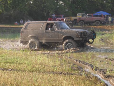 1993 Ford Bronco - A muddy SUV navigates a challenging off-road course with other vehicles and spectators in the background.