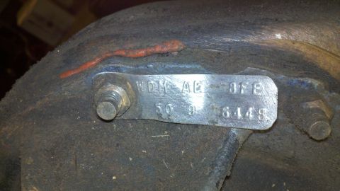 1978 Ford Bronco - A close-up view of a metal identification tag attached to a rusty mechanical part, showing stamped alphanumeric characters.