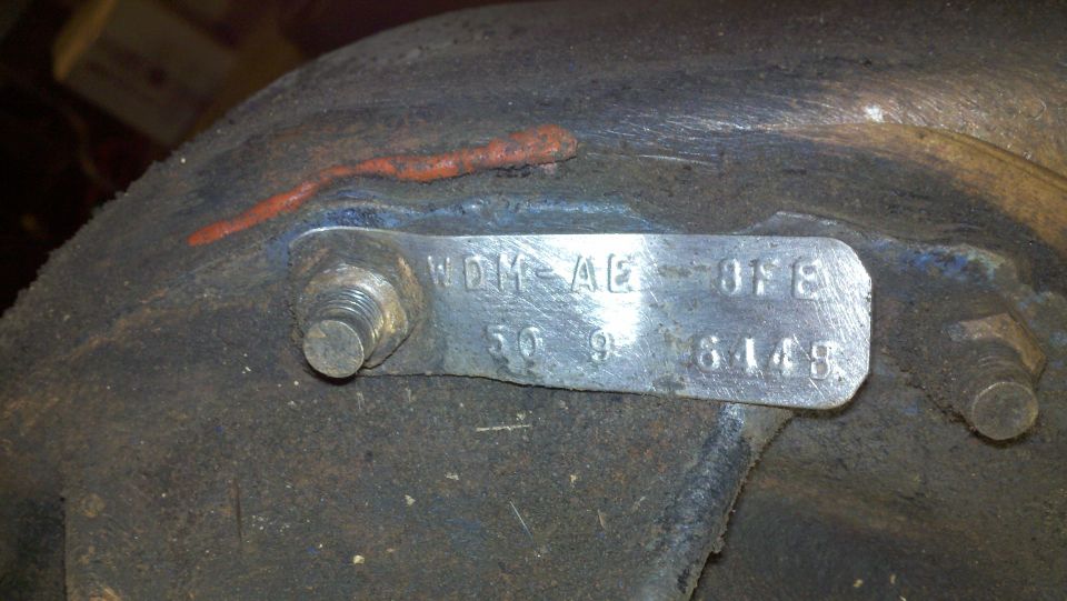Metal identification tag with numbers and letters on a rusty component