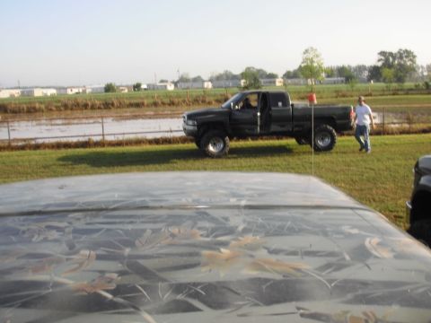 1993 Ford Bronco - A man stands near a lifted pickup truck next to a flooded area under a bright sky.